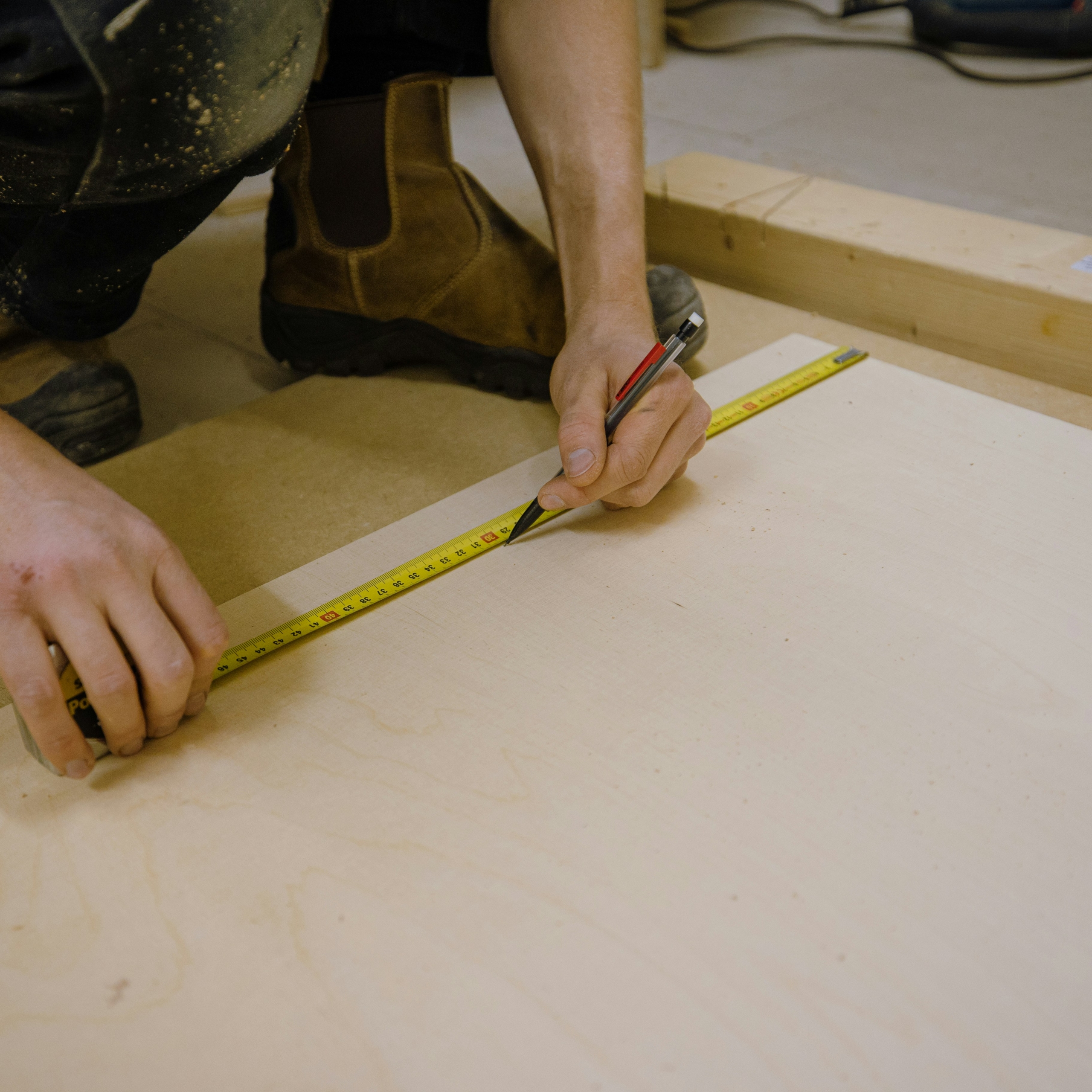 A carpenter marking measurements on a wooden board using a tape measure and pencil