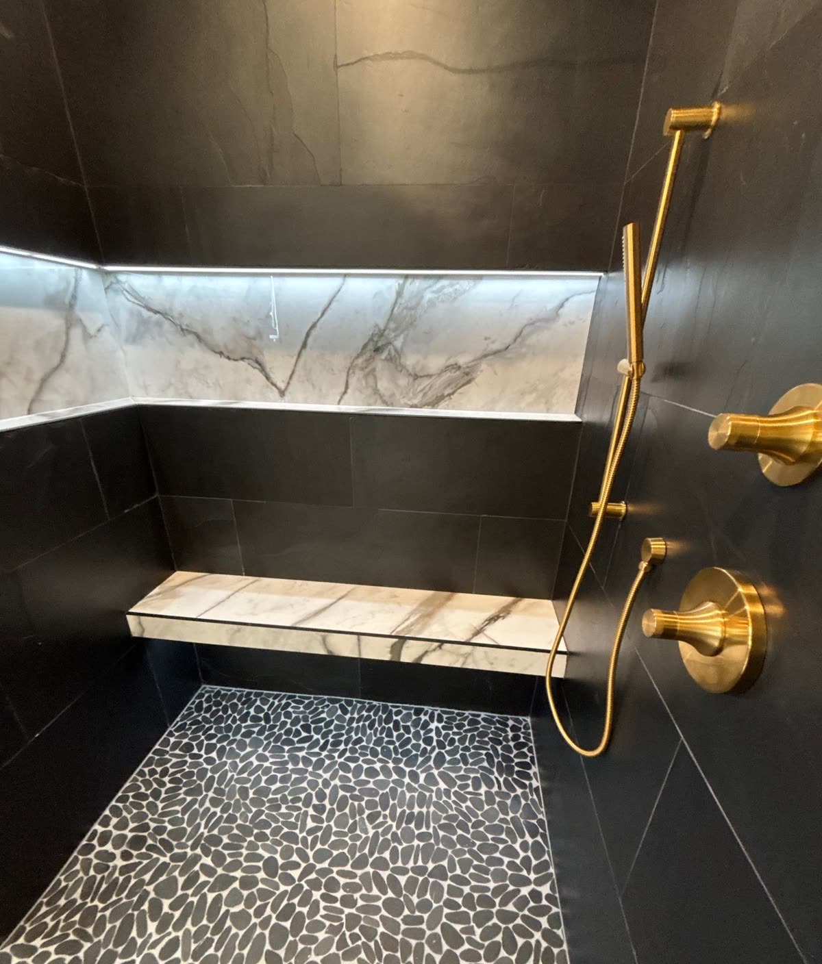 Walk-in shower with a backlit marble niche, floating stone bench, and unlacquered brass fittings