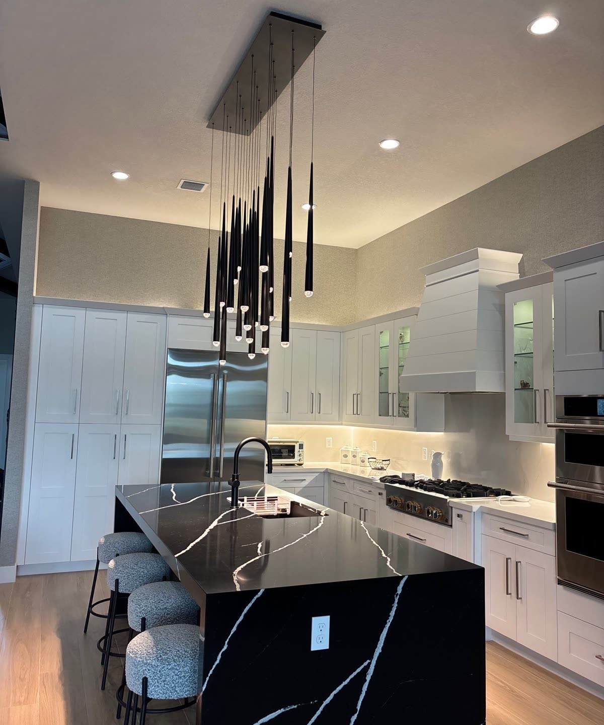 Custom kitchen remodel in Palm Beach Gardens with white shaker cabinetry, a black quartz waterfall island and a cascading pendant cluster, built by H&H Signature Renovations